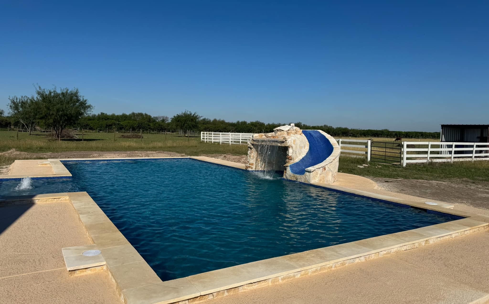 Resort-style pool with a stone waterfall and tile slide on open South Texas ranch land